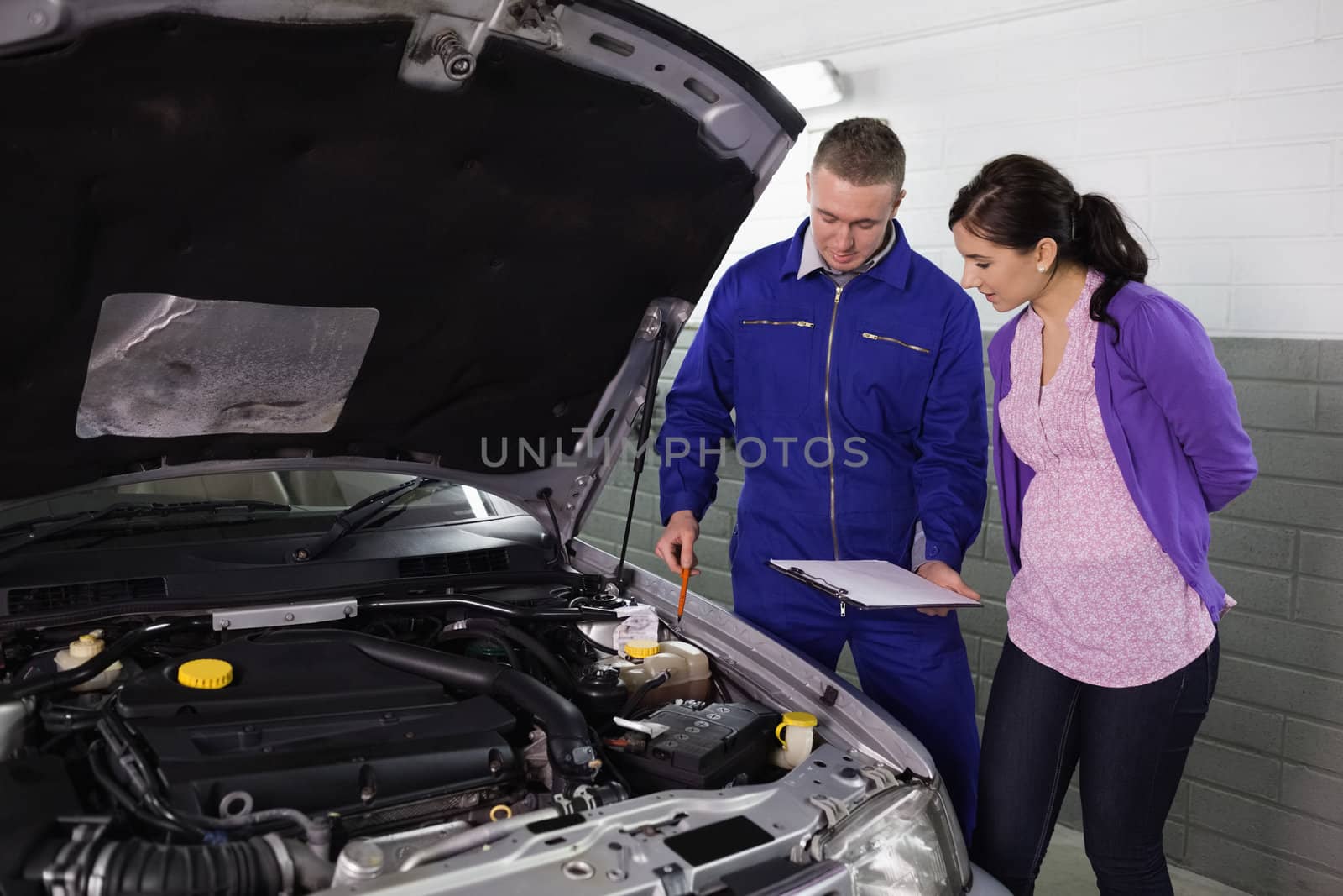 Mechanic showing a par of the engine to a woman in a garage