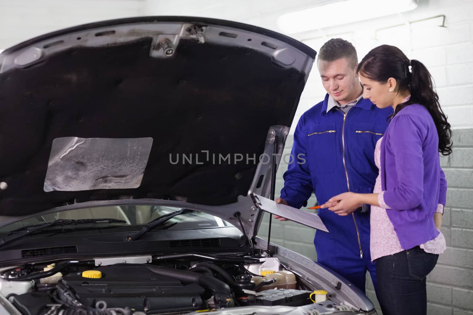 Mechanic standing with a clipboard next to a client in a garage