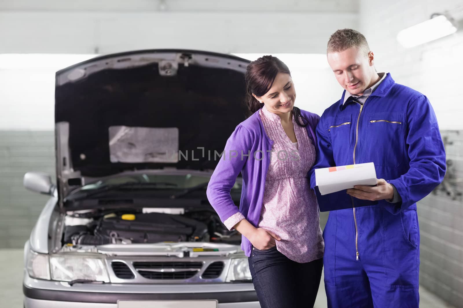 Mechanic showing a paper in a clipboard to a woman in a garage