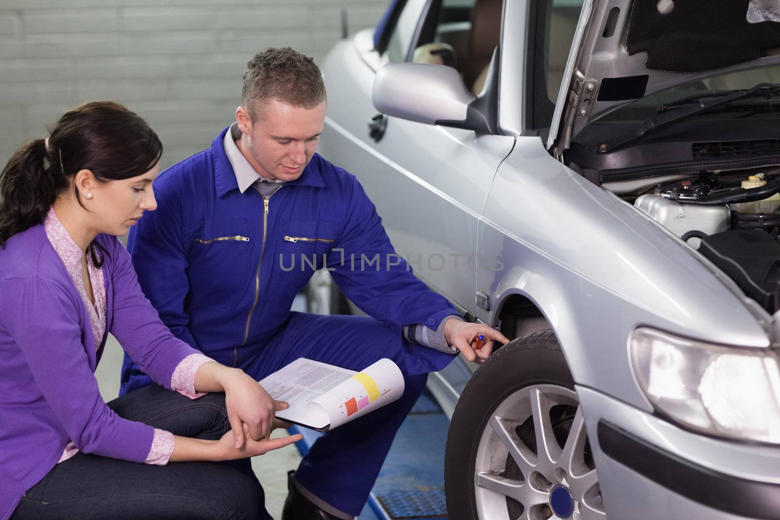 Mechanic showing the car wheel to a woman in a garage