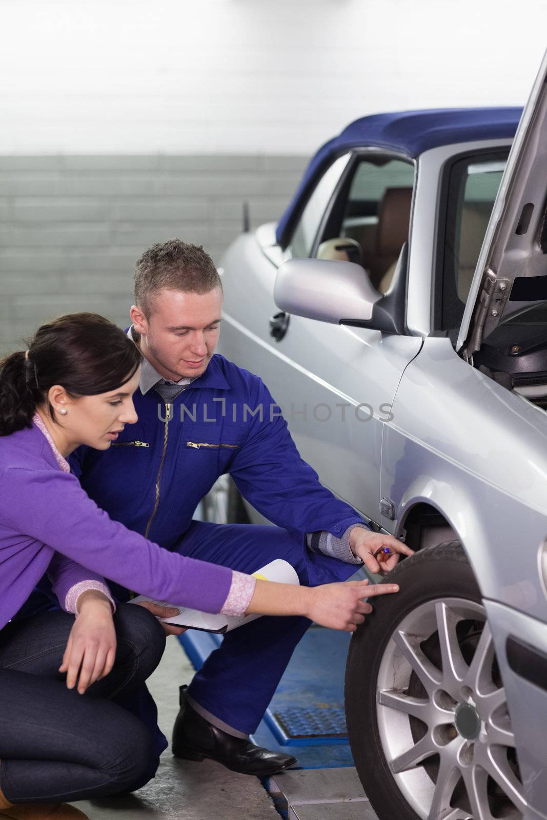 Mechanic touching the car wheel next to a woman by Wavebreakmedia