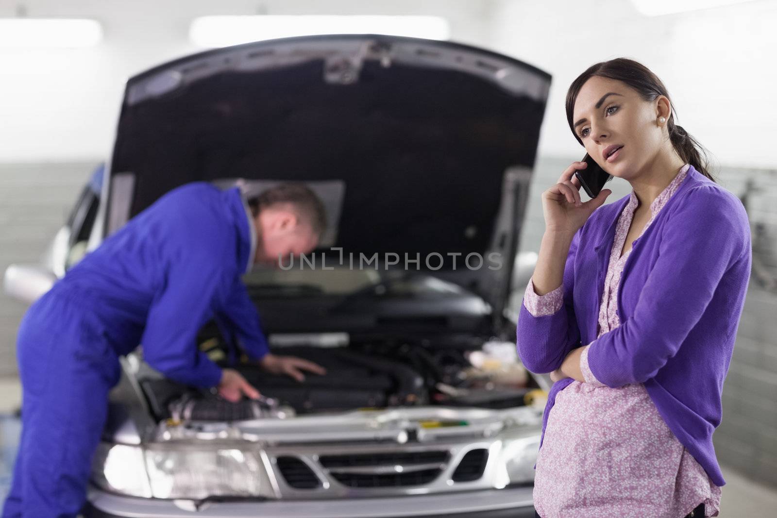 Woman calling next to a mechanic in a garage