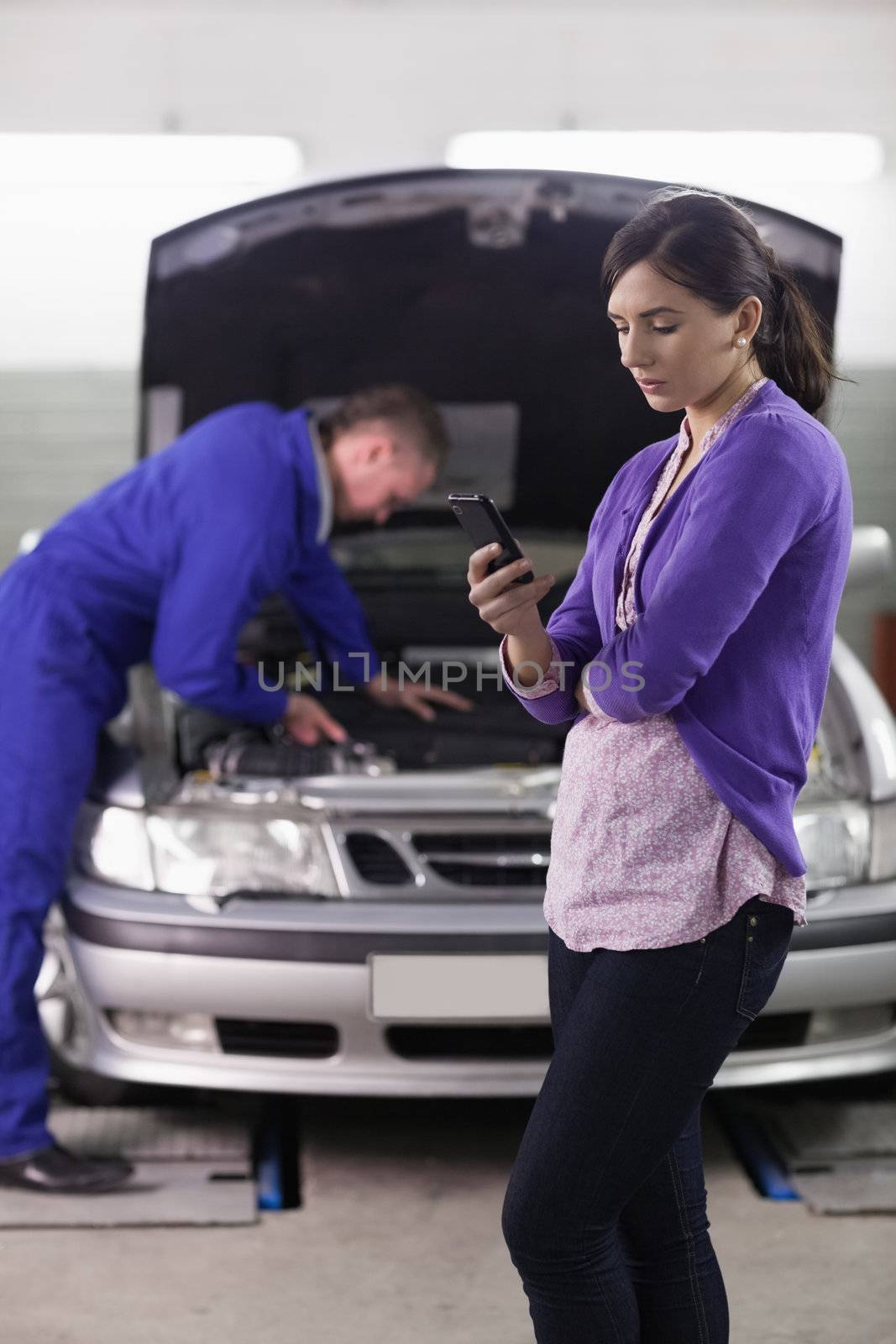 Woman looking a her mobile phone next to a mechanic in a garage