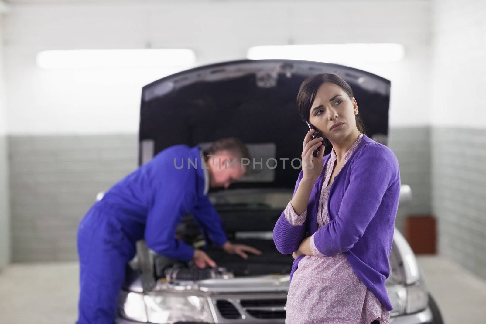 Client holding a mobile phone next to a car in a garage