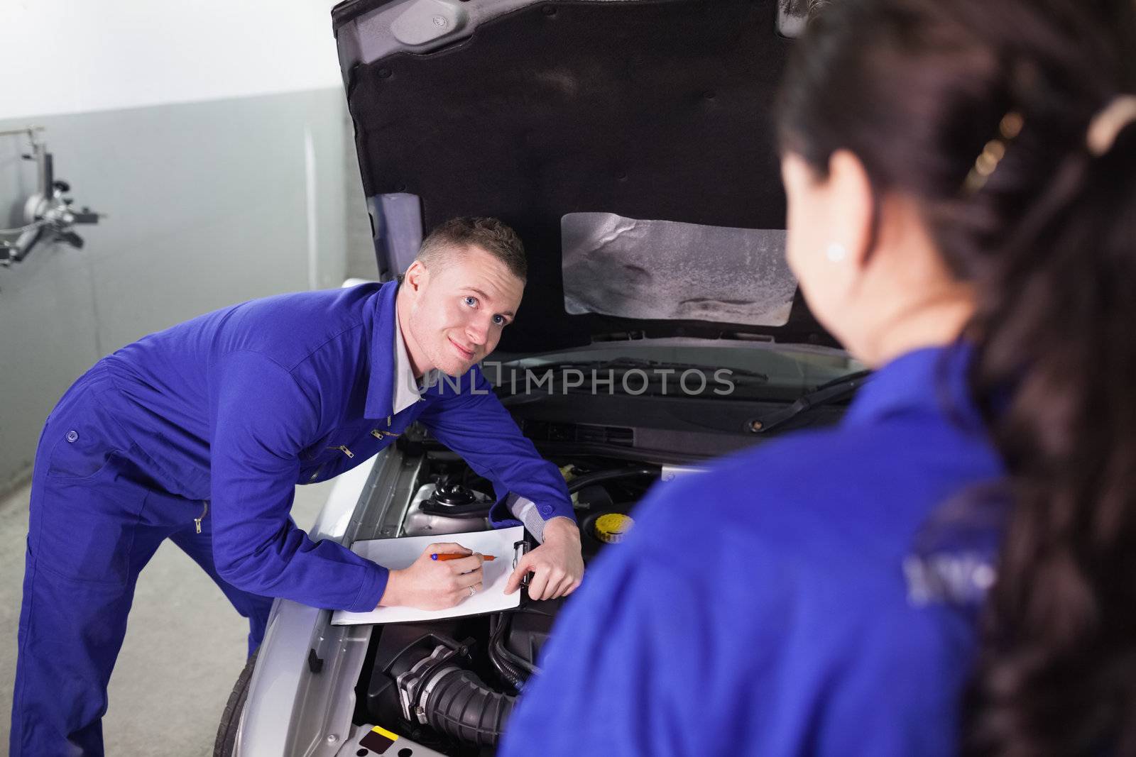 Mechanic leaning on a car looking at a colleague in a garage