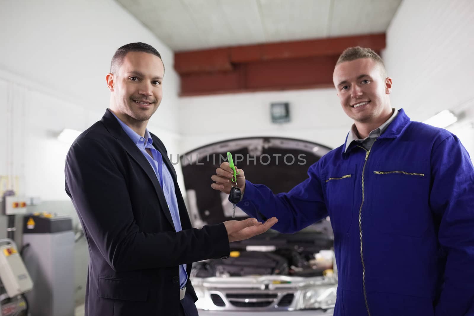 Mechanic smiling while giving car key to a man in a garage