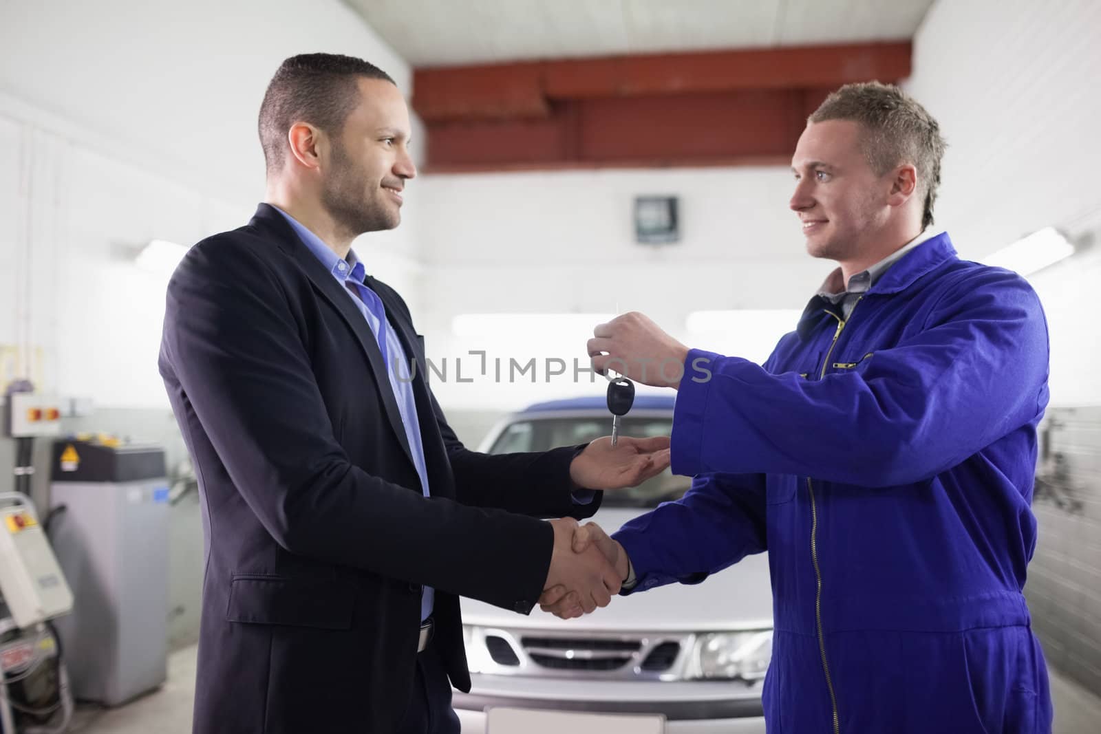 Man receiving car key while shaking hand to a mechanic in a garage