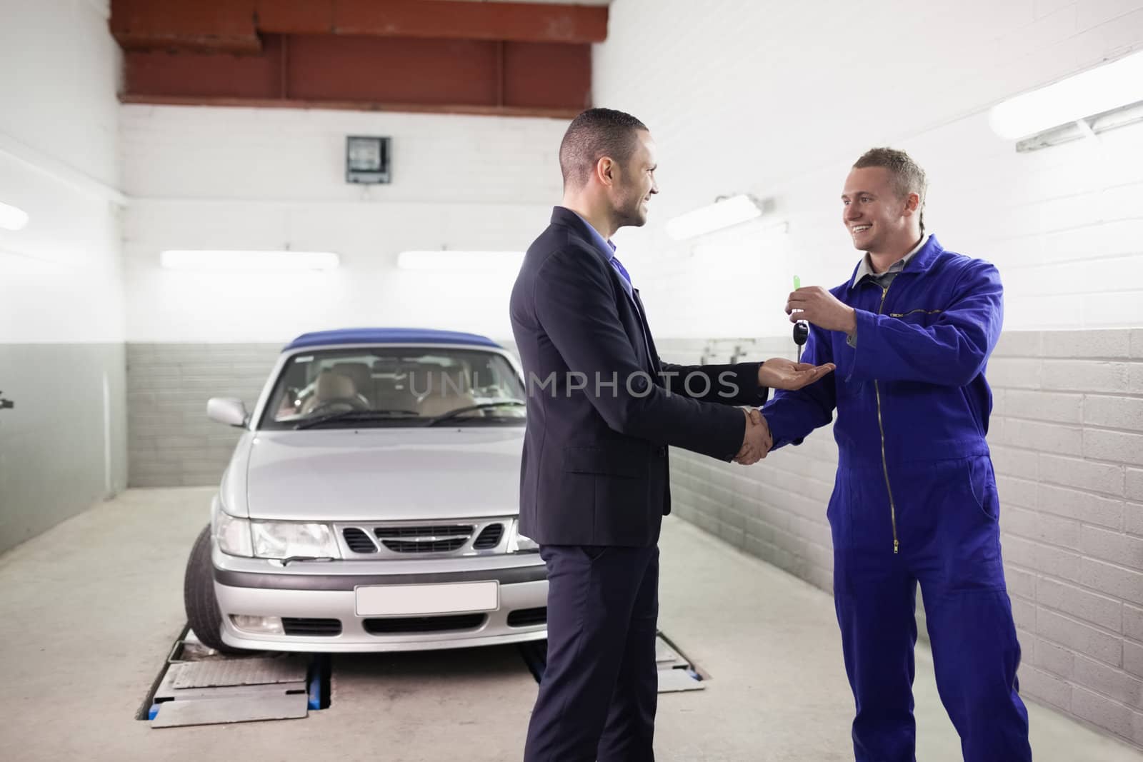 Mechanic giving car key while shaking hand to a client in a garage