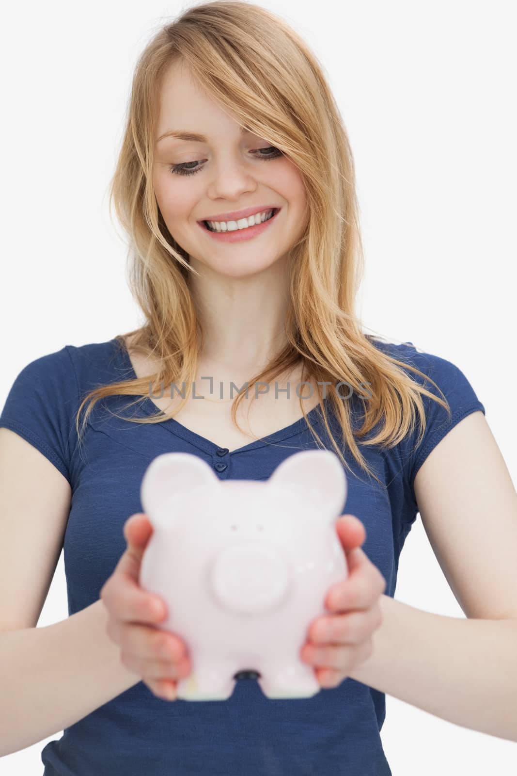 Blonde woman holding a piggy bank while looking it against a white background