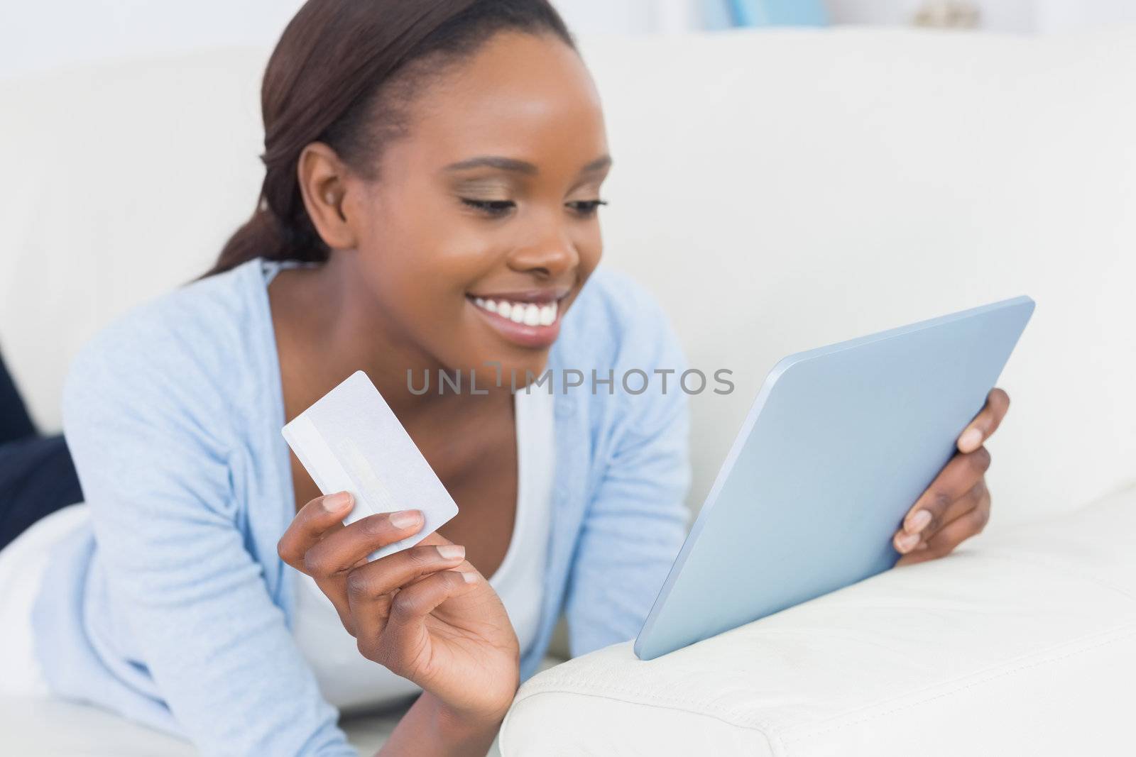 Black woman lying on front holding a credit card in a living room