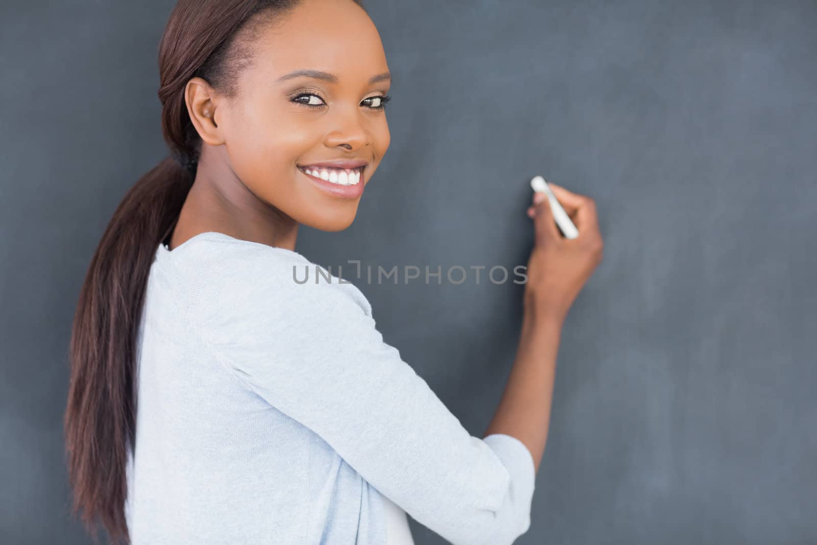 Black woman smiling while holding a chalk in a classroom