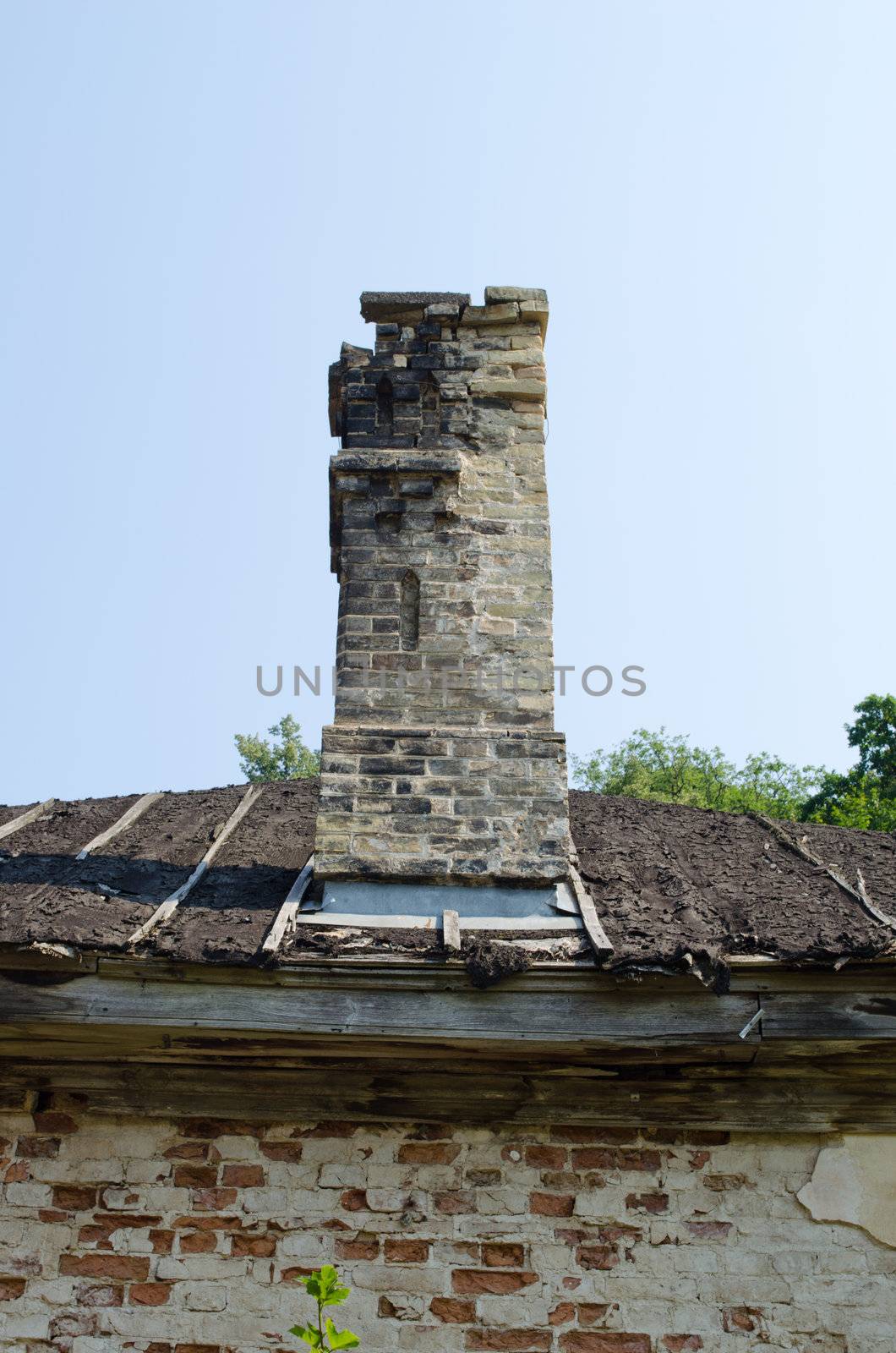 Ancient collapsing building wall roof and chimney on background of blue sky.
