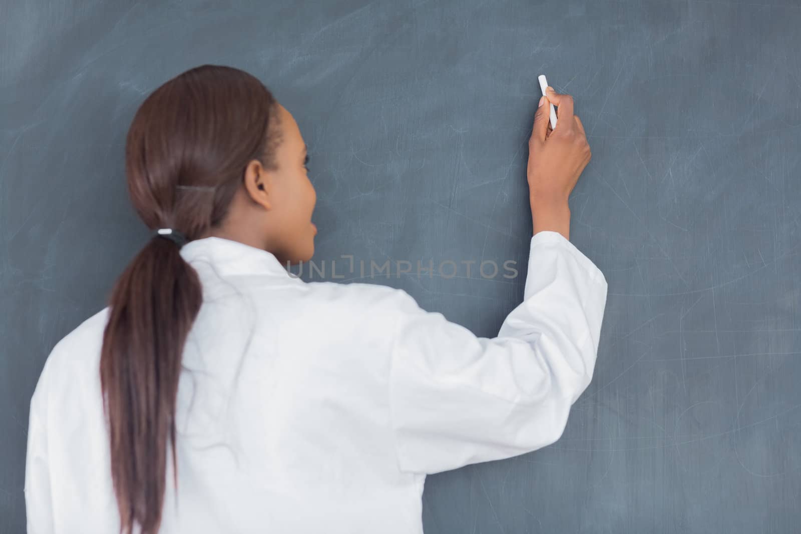 Teacher smiling while writing on a blackboard in a classroom