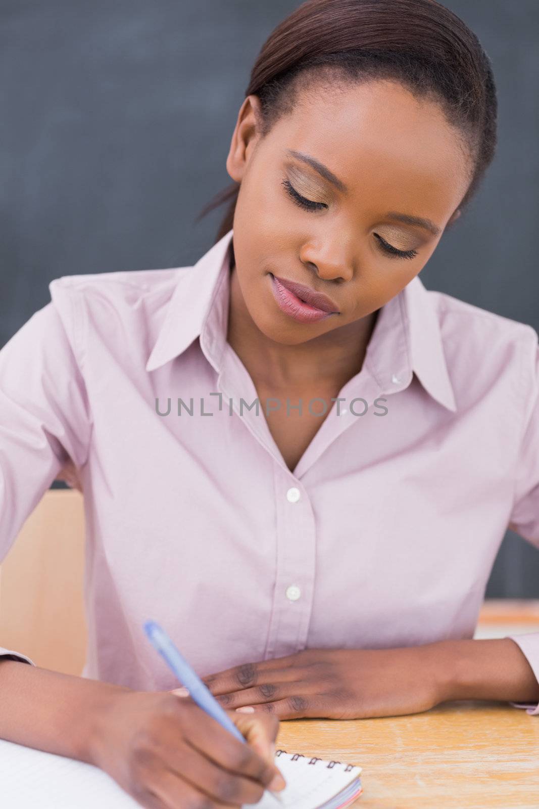 Black teacher writing on a notebook in a classroom