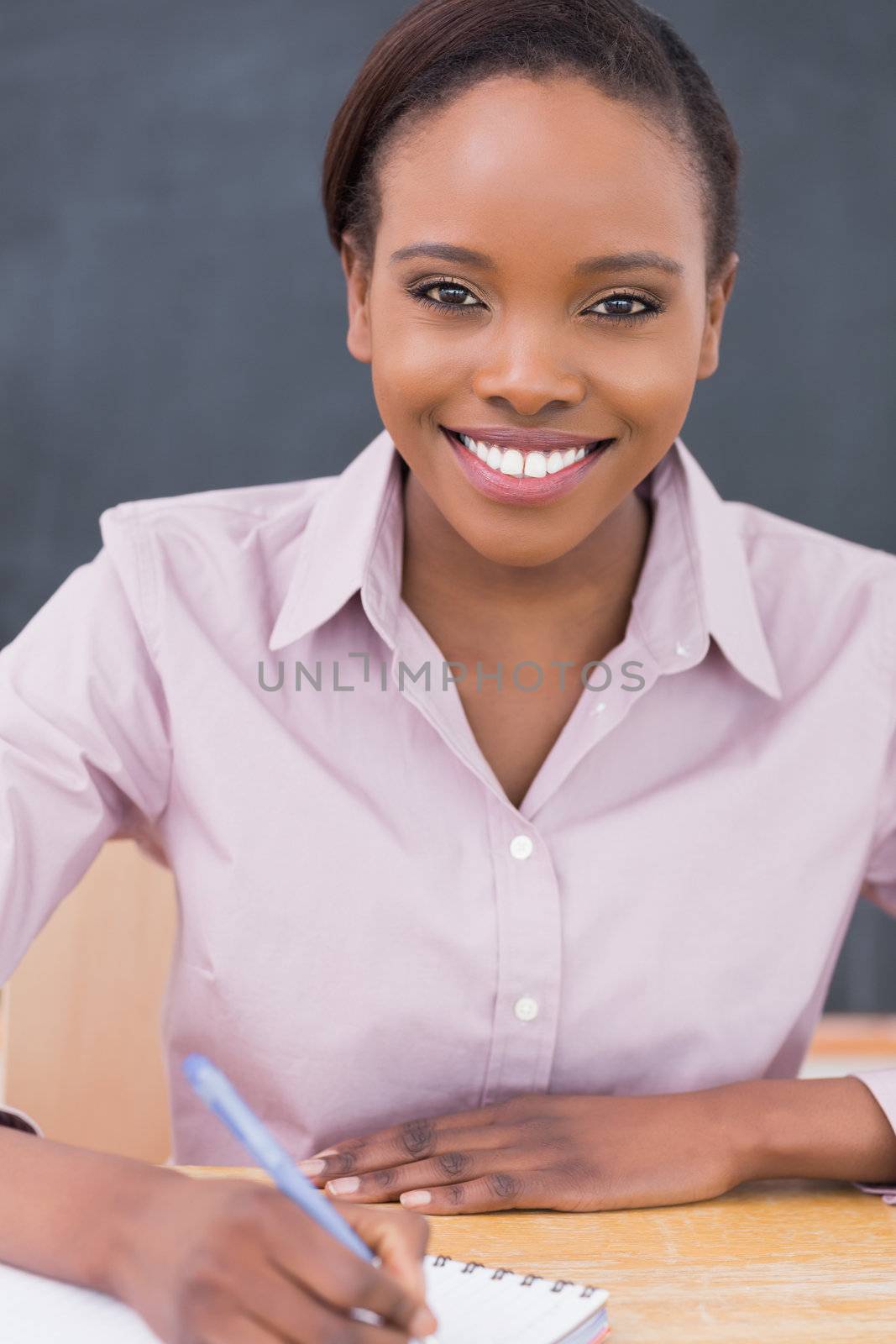 Smiling teacher writing on a notebook in a classroom