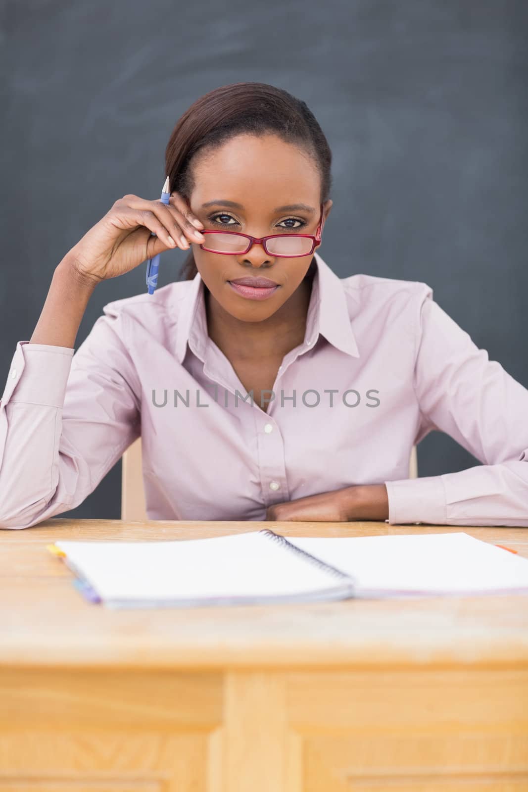Teacher sitting at desk while touching her glasses in a classroom