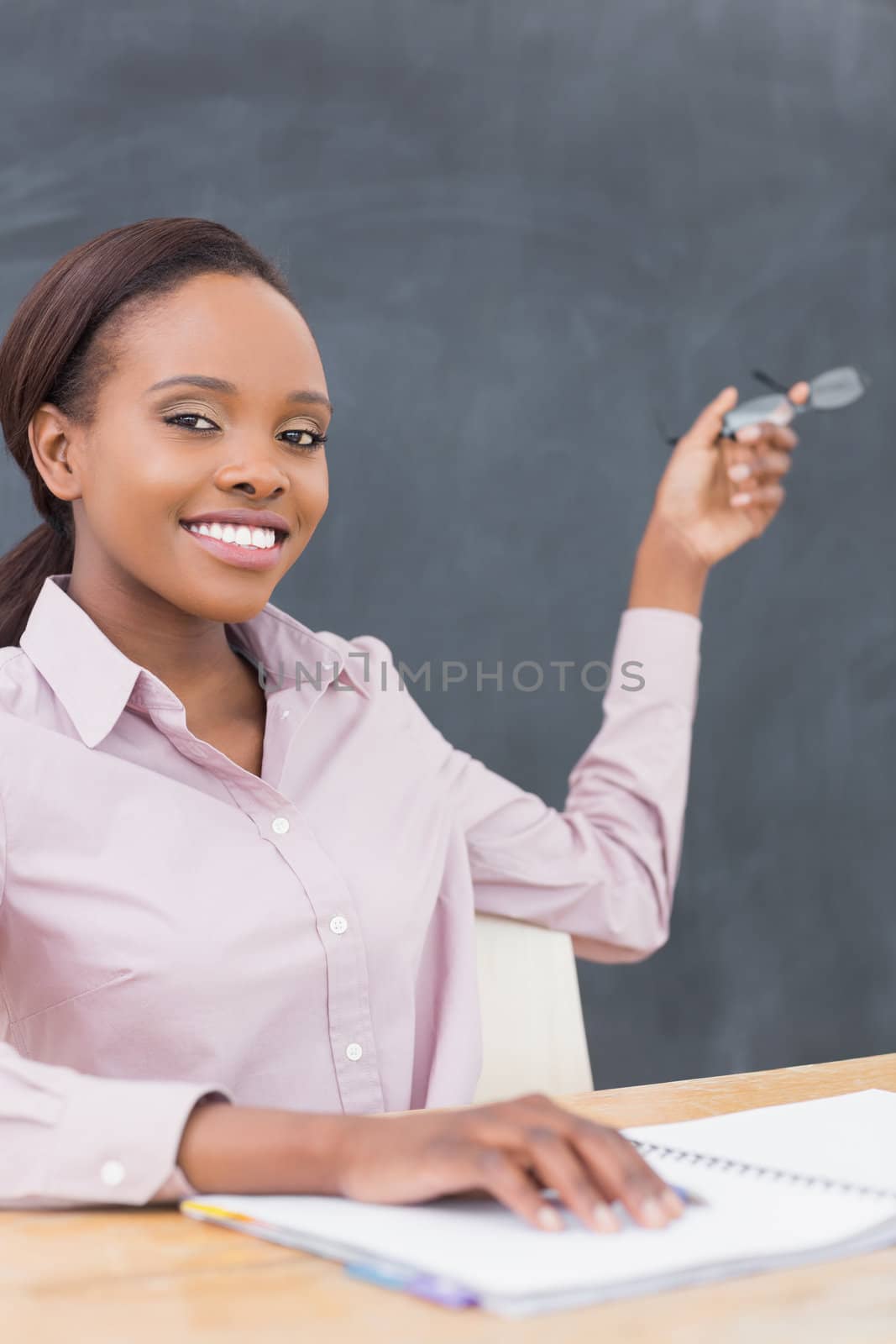 Smiling teacher showing the blackboard with her glasses in a classroom
