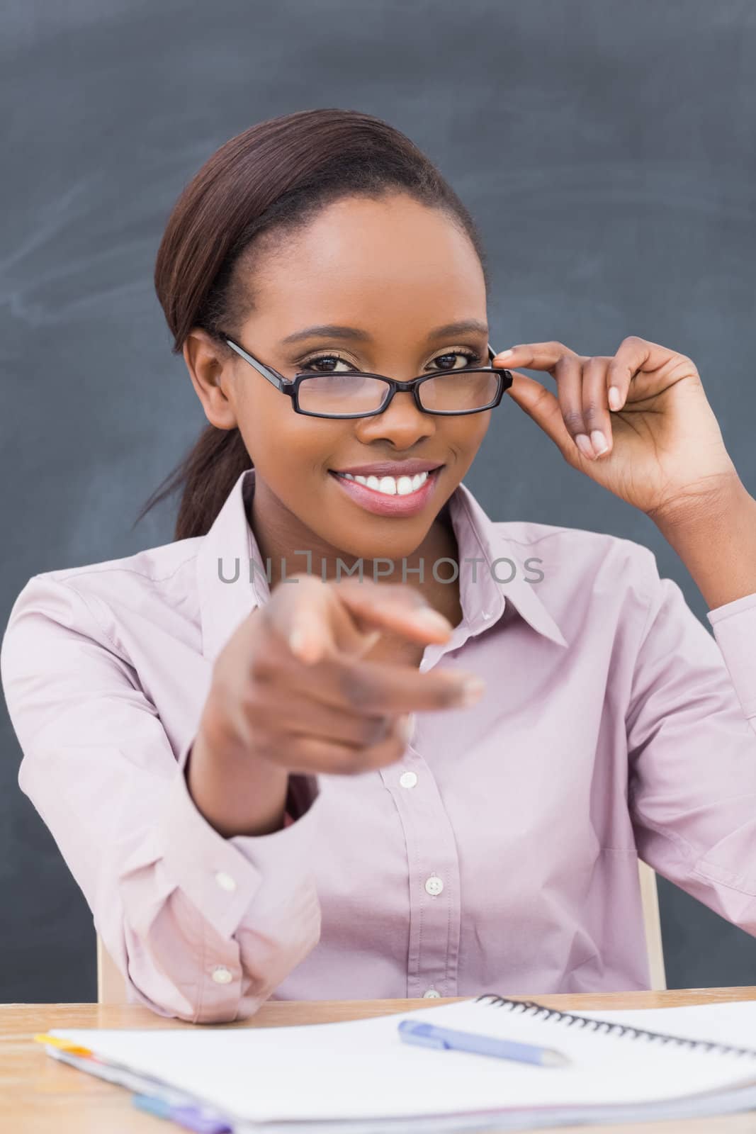 Teacher touching her glasses while sitting at desk in a classroom