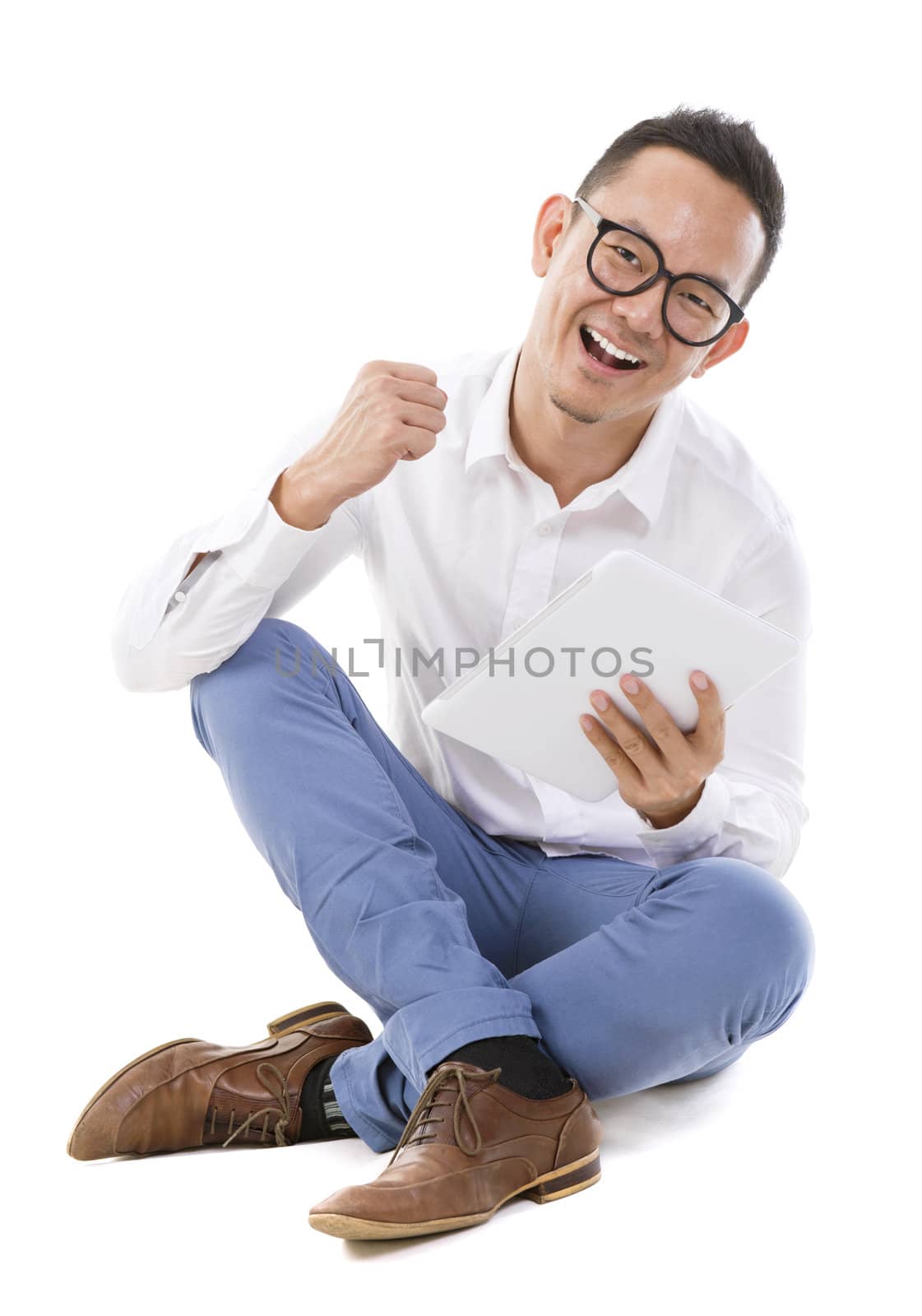 Fullbody happy Asian man sitting on floor using tablet computer
