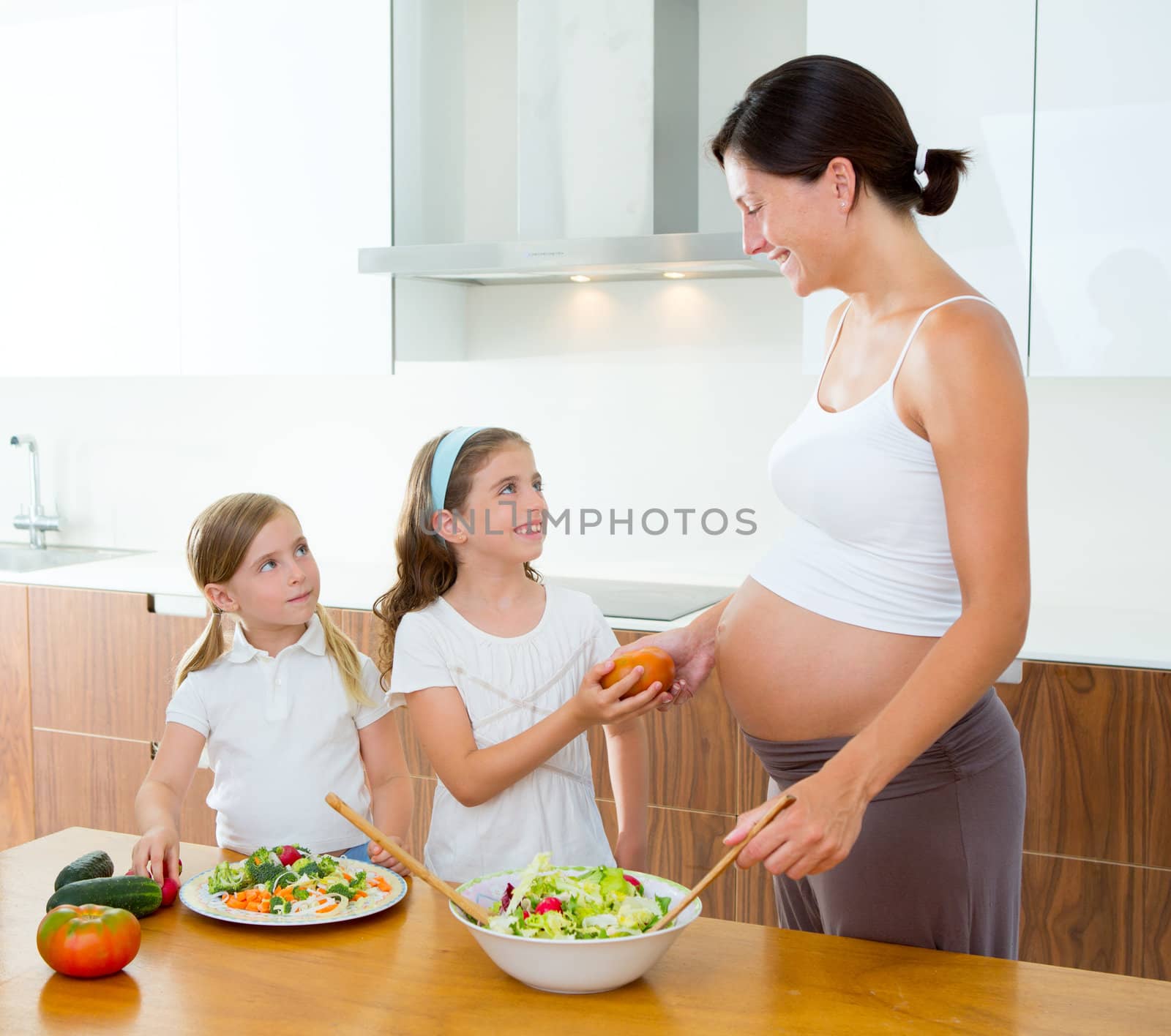 Beautiful pregnant mother with her daughters at kitchen preparing salad