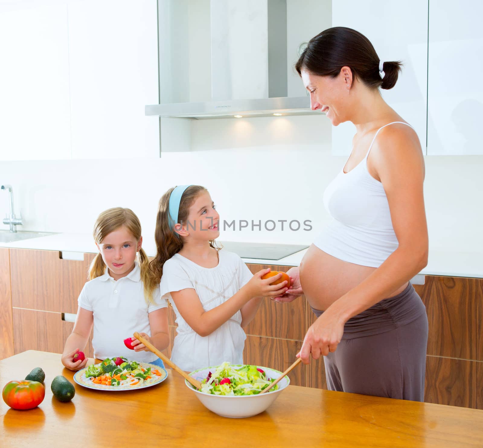 Beautiful pregnant mother with her daughters at kitchen preparing salad