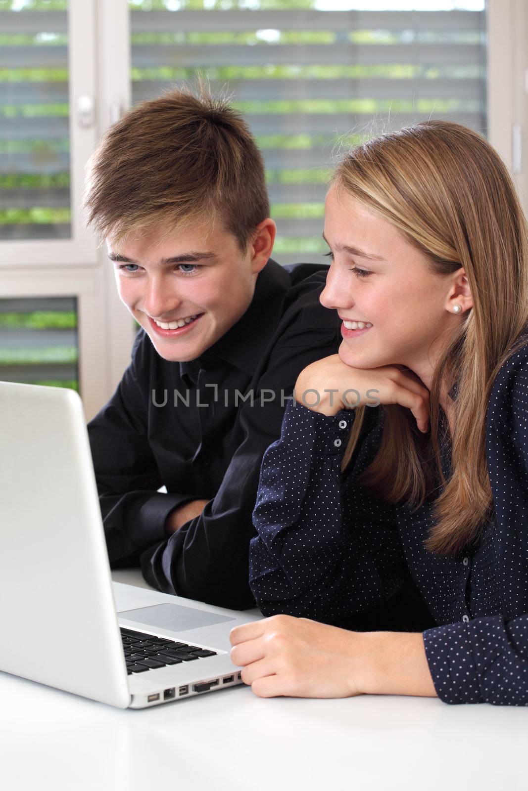 Photo of a young female and male smiling and working with a laptop in their highschool classroom. Focus on female face.