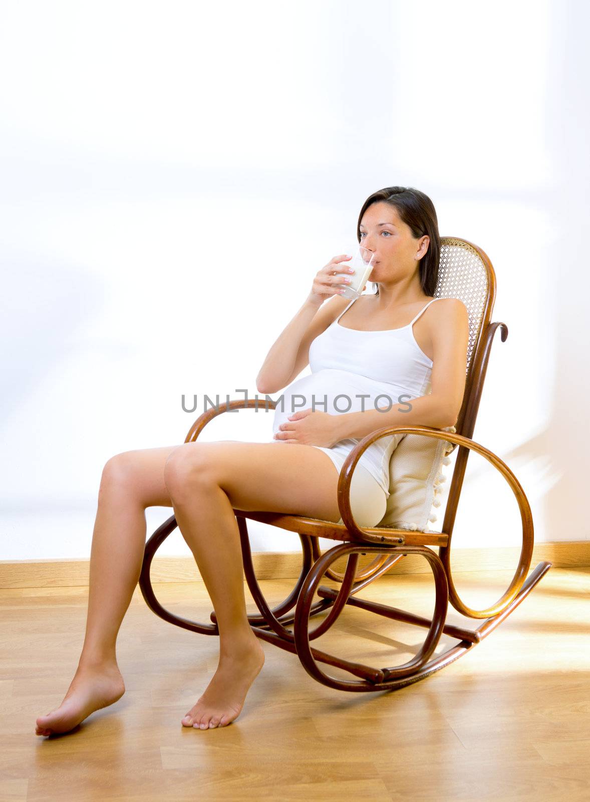 Beautiful pregnant woman drinking milk at home on rocker chair