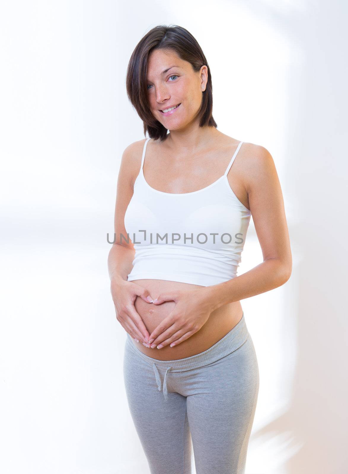 Beautiful pregnant woman love heart shape symbol on belly with fingers