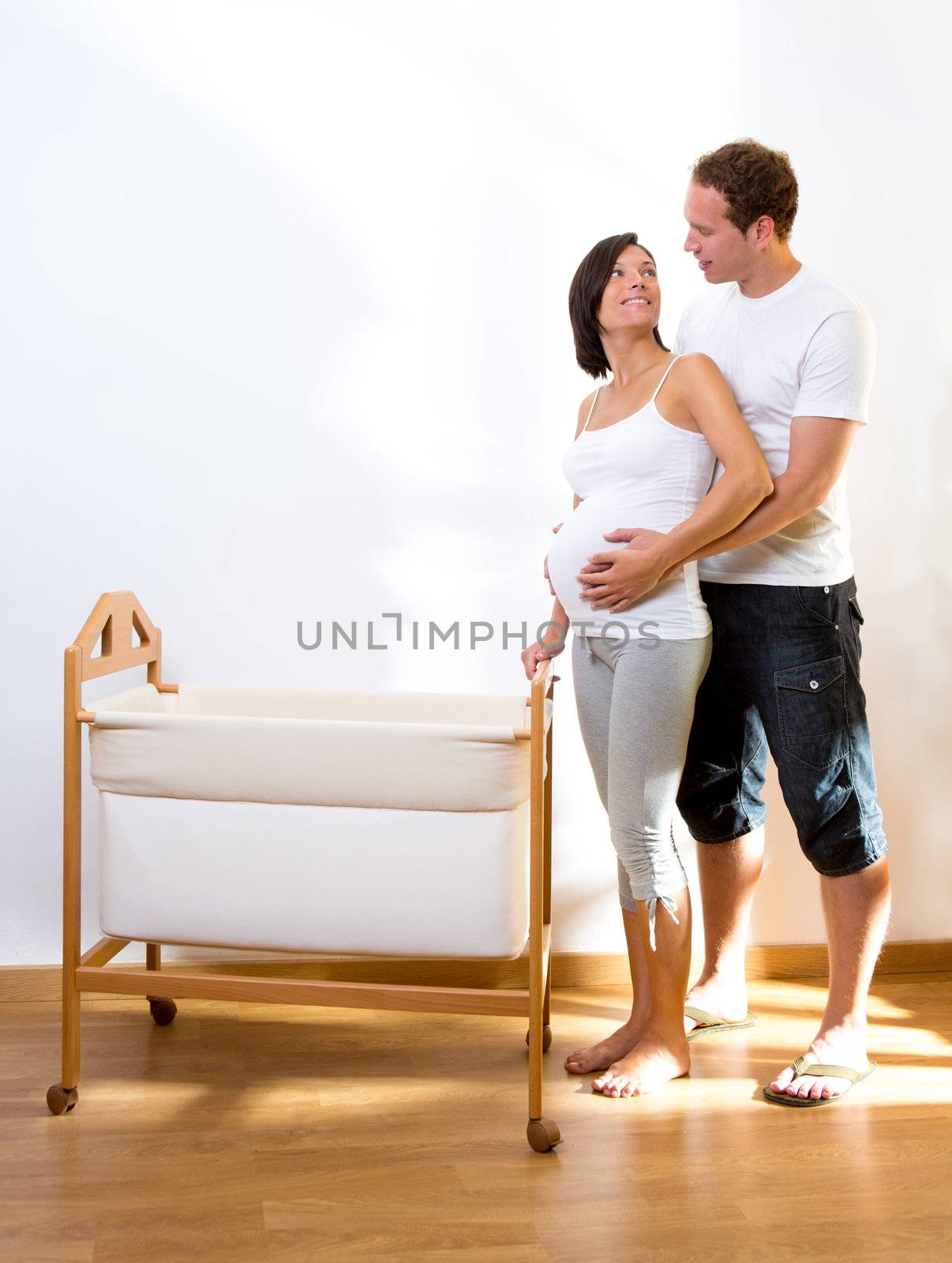Couple with pregnant woman hug with baby cradle at home
