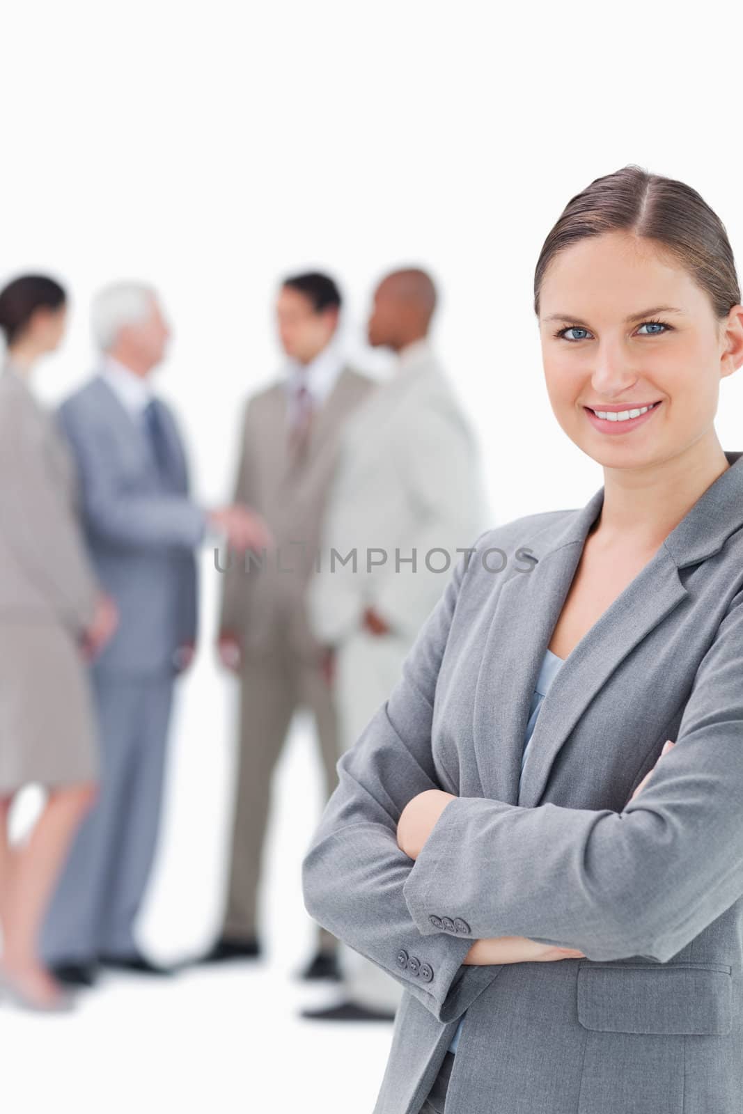 Smiling saleswoman with arms folded and colleagues behind her against a white background