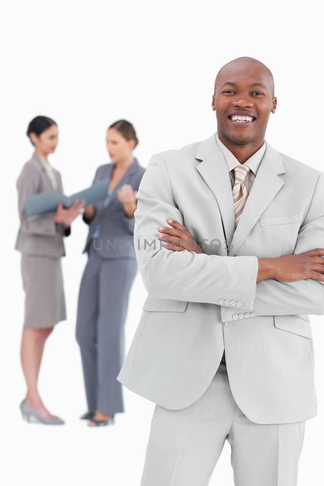 Smiling businessman with arms crossed and colleagues behind him against a white background