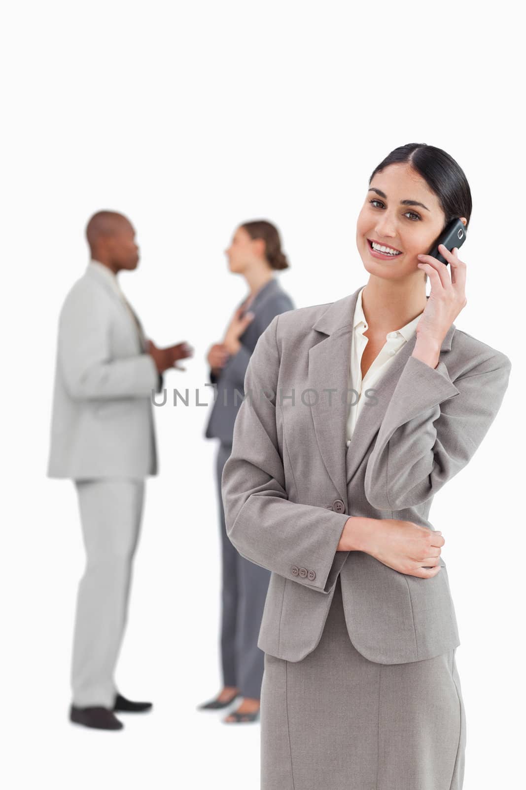 Smiling saleswoman with cellphone and colleagues behind her against a white background