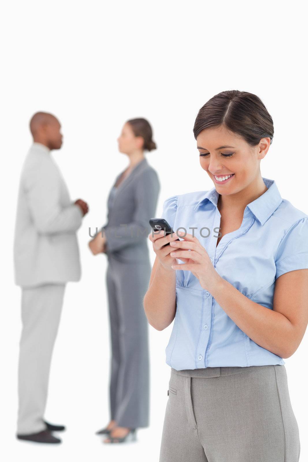Businesswoman looking at cellphone with associates behind her against a white background