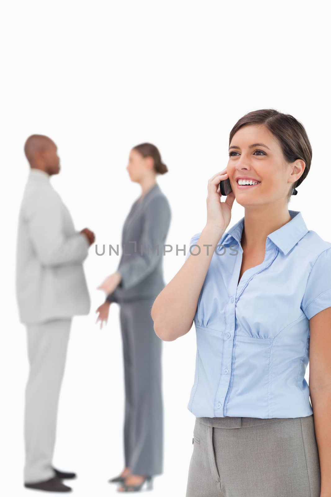 Smiling saleswoman on the phone with colleagues behind her against a white background