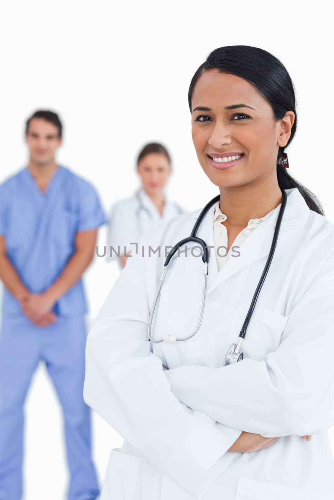 Smiling doctor with arms folded and staff behind her against a white background