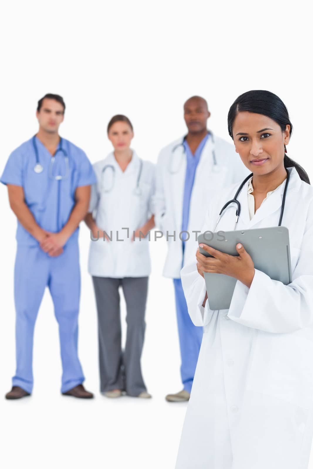 Female doctor with clipboard and colleagues behind her by Wavebreakmedia