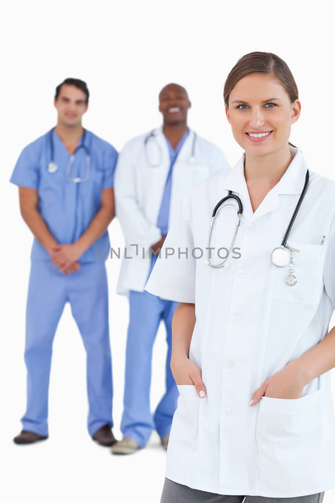 Smiling female doctor with male colleagues behind her against a white background