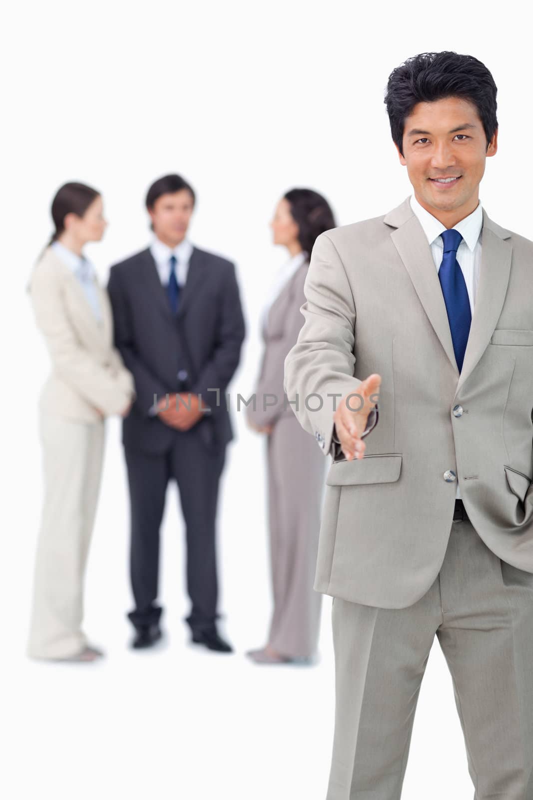 Businessman with colleagues behind him extending his hand against a white background