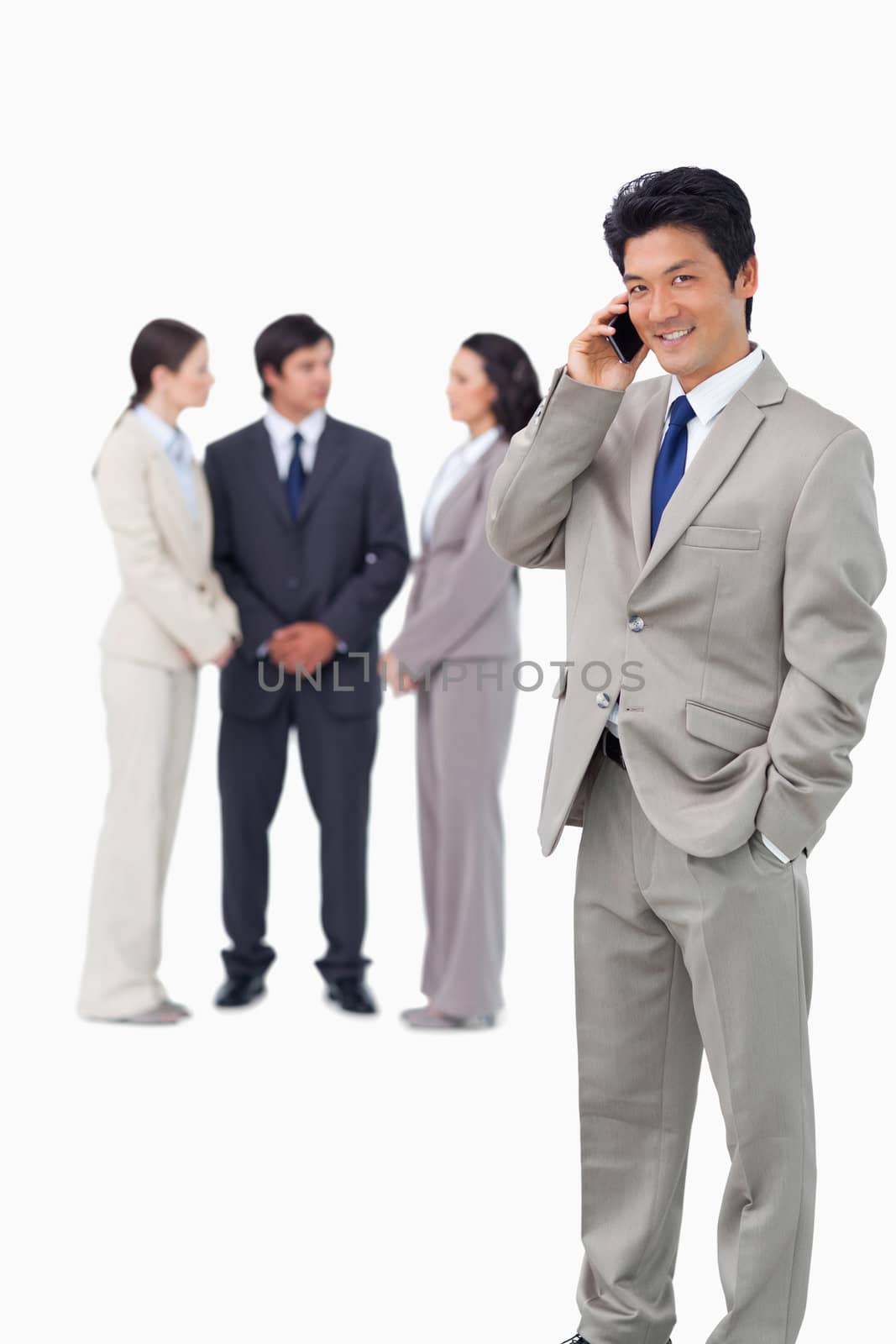 Businessman on cellphone with colleagues behind him against a white background