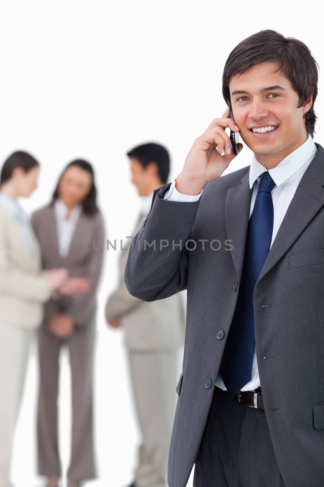 Smiling salesman on cellphone with team behind him against a white background