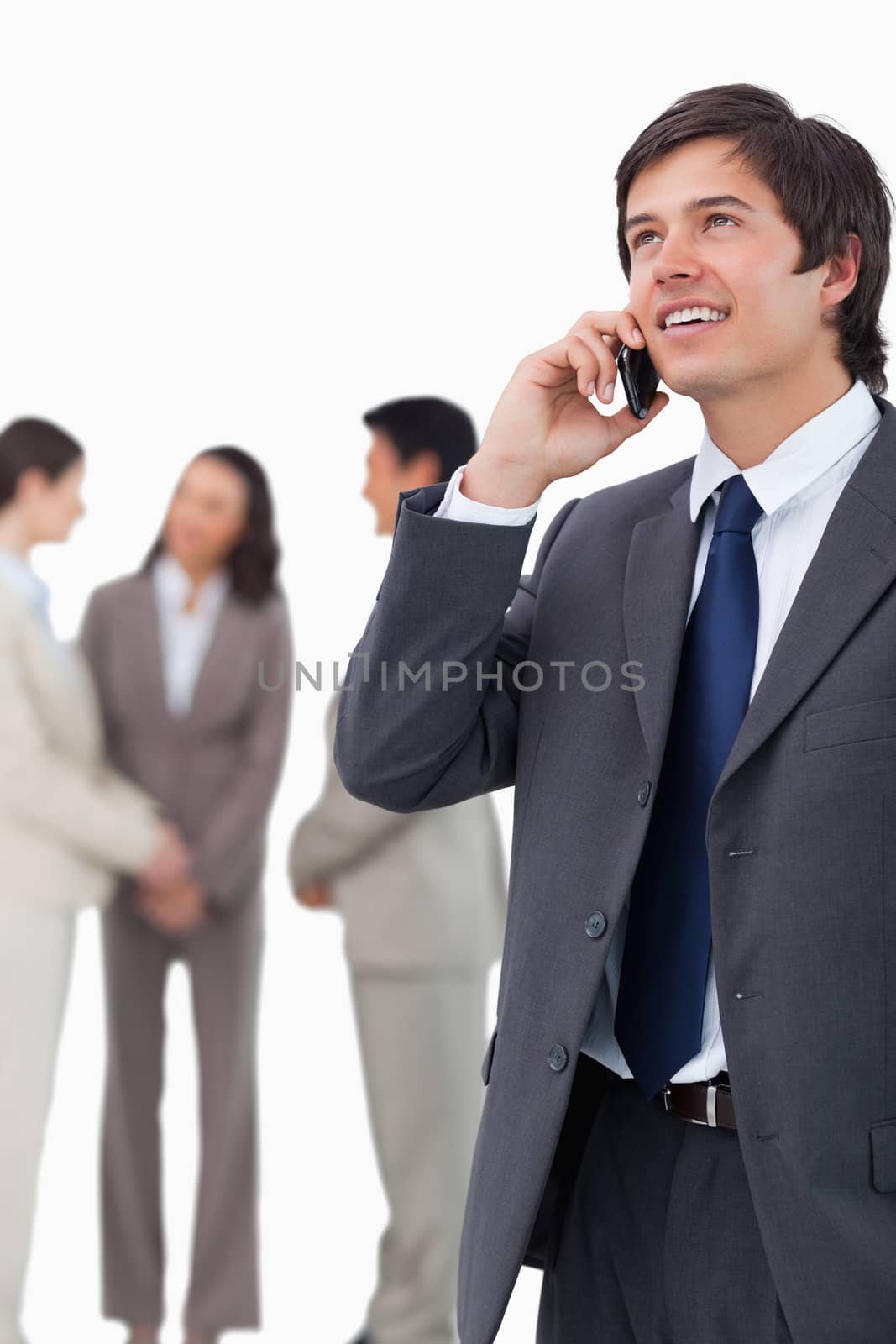 Salesman talking on mobile phone with team behind him against a white background