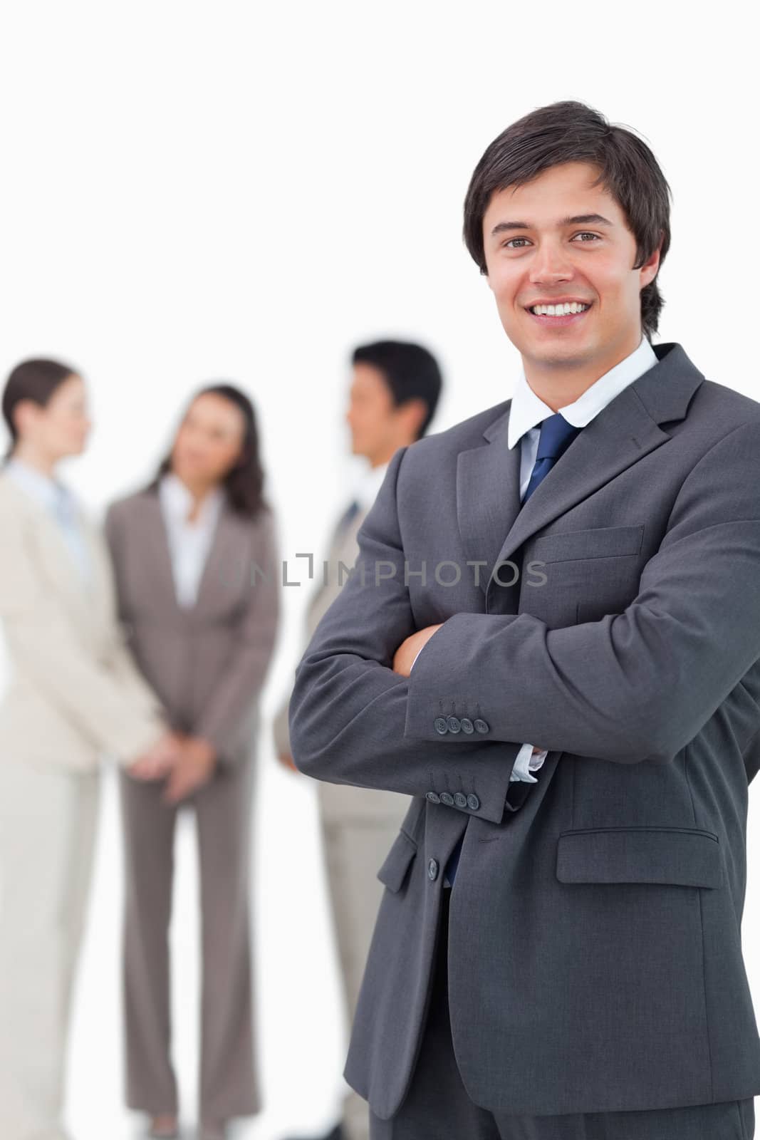 Smiling salesman with arms crossed and team behind him against a white background