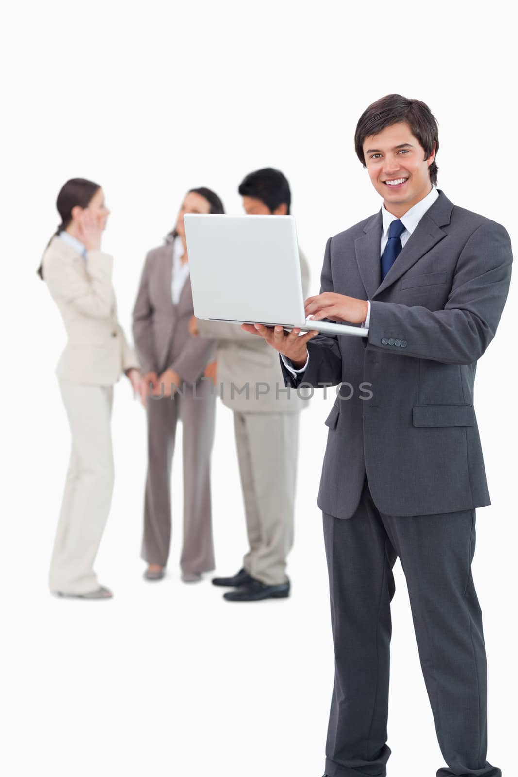 Smiling salesman with laptop and team behind him against a white background