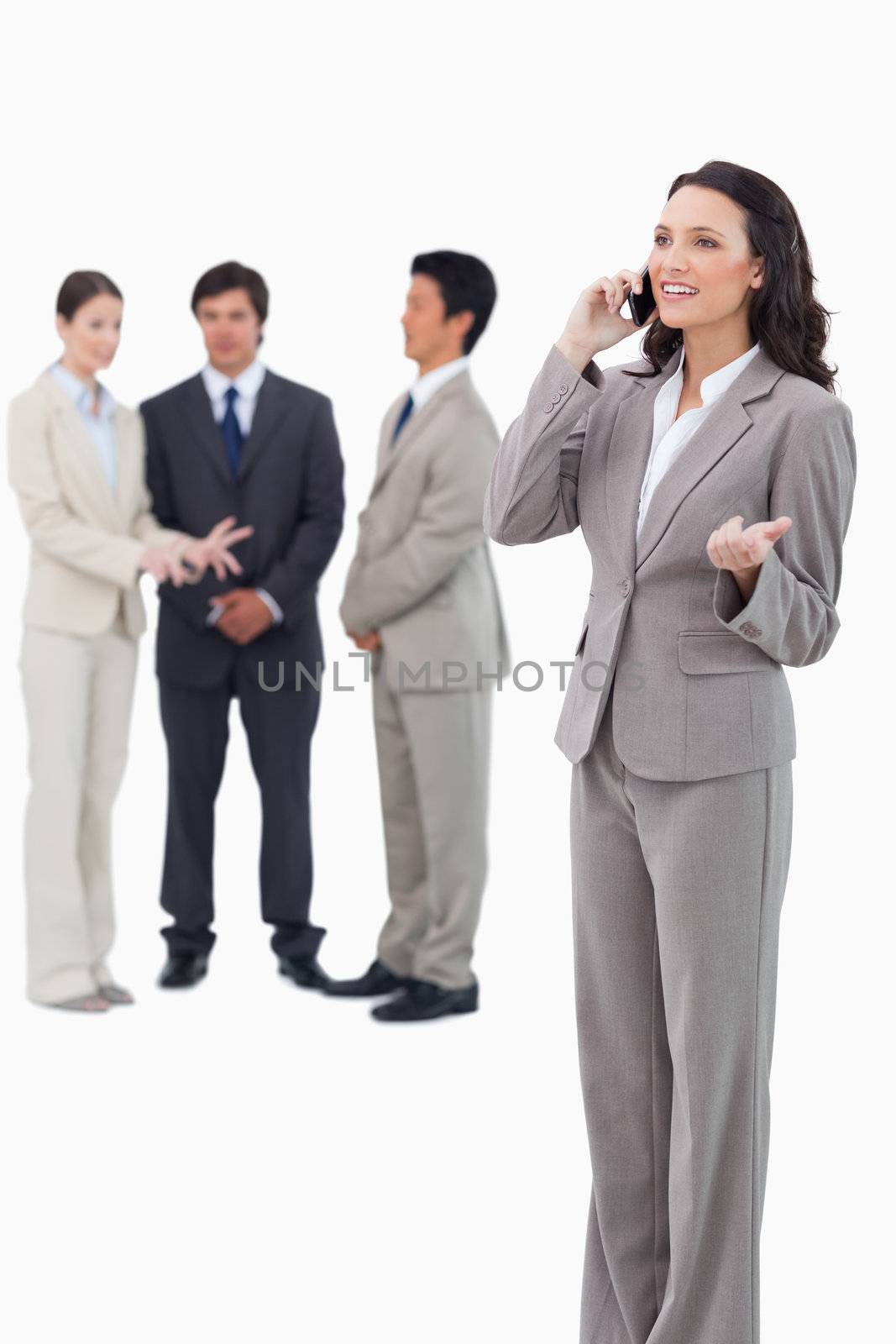 Saleswoman talking on cellphone with colleagues behind her against a white background
