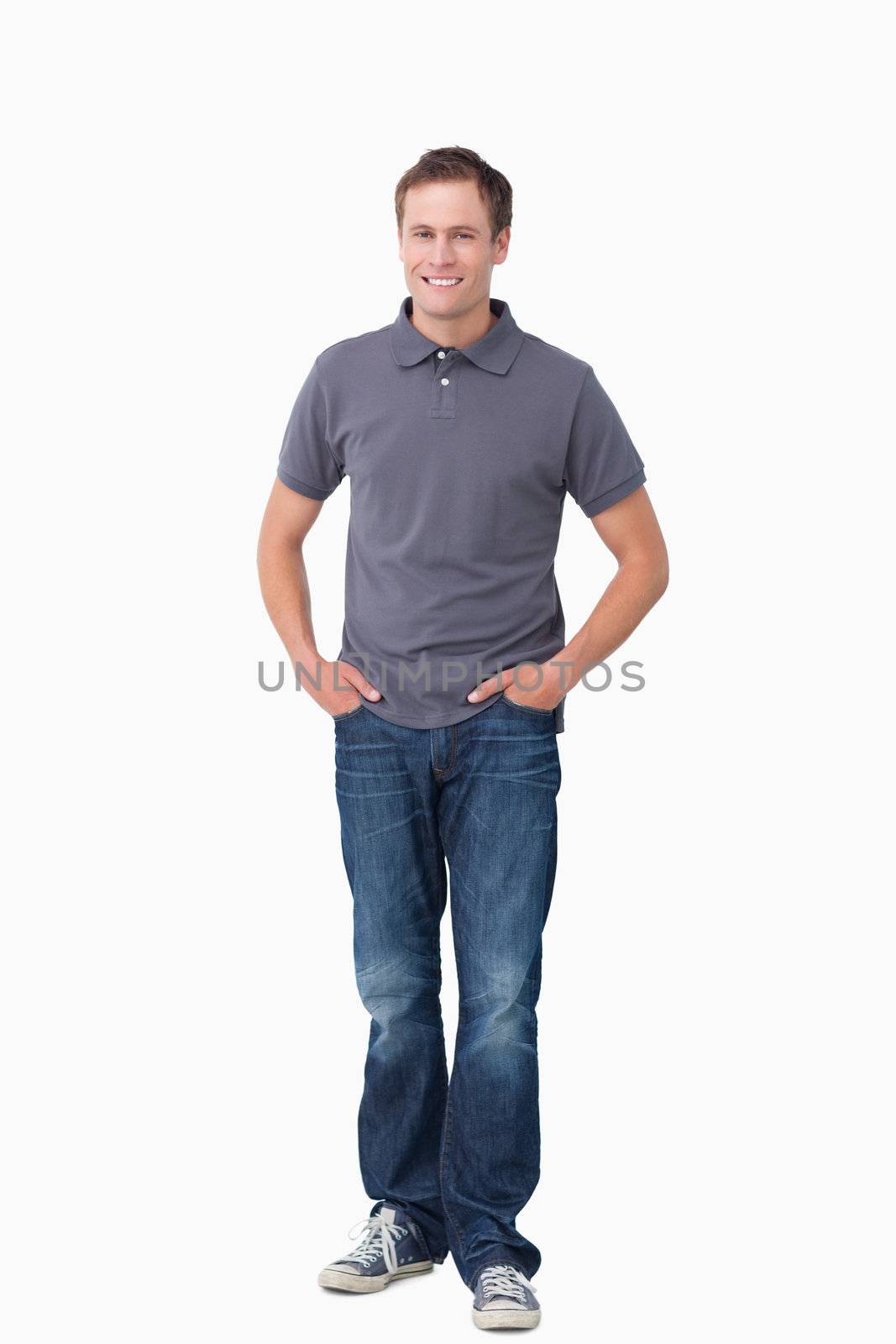Smiling young man with hands in his pockets against a white background