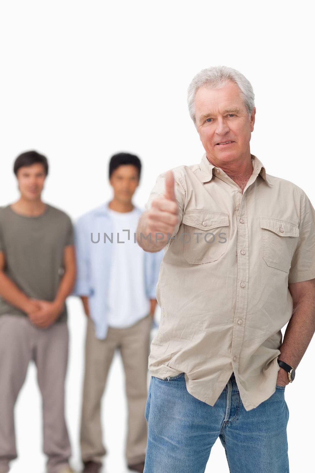 Senior man giving thumb up with young people behind him against a white background