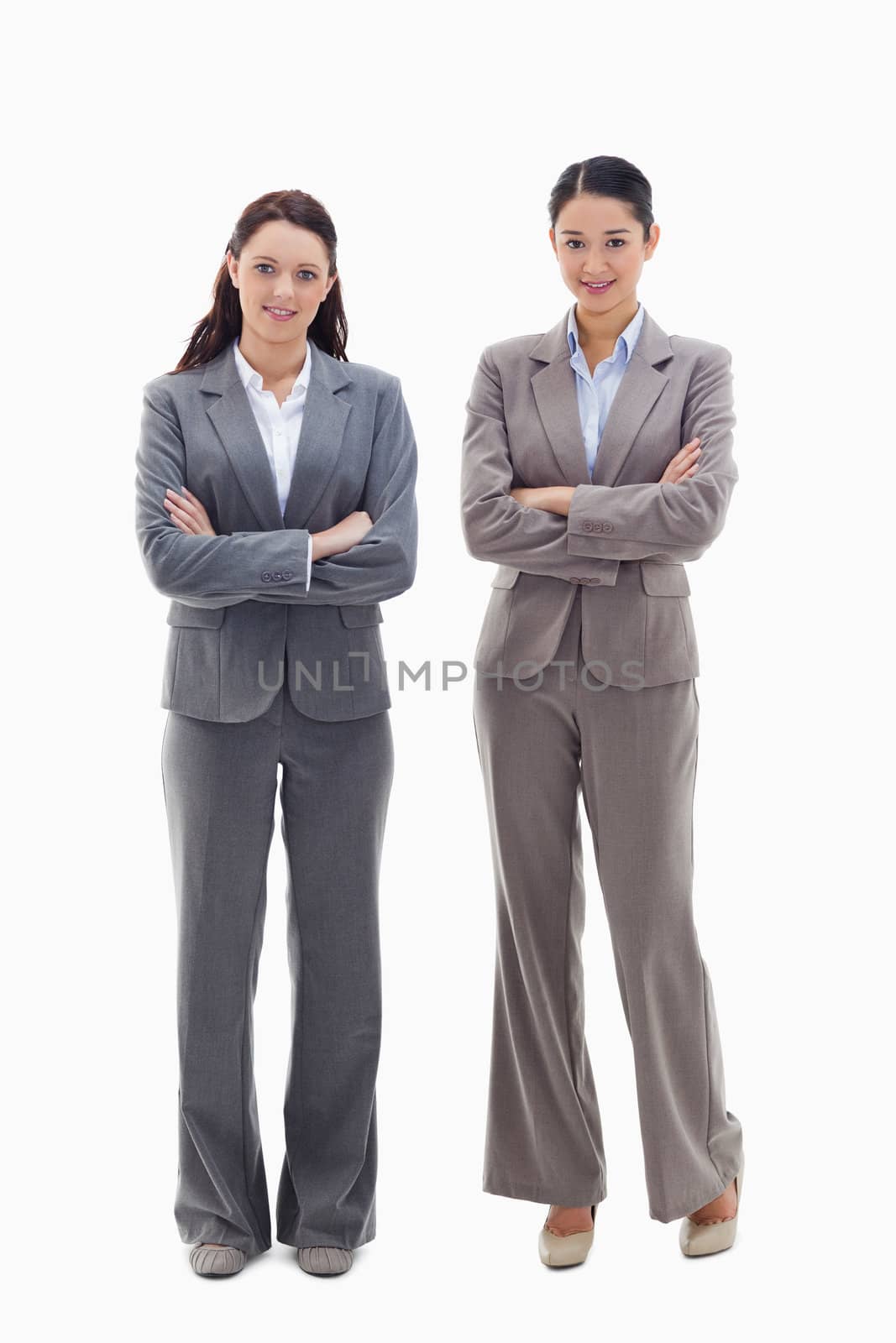 Two businesswomen smiling and crossing their arms against white background