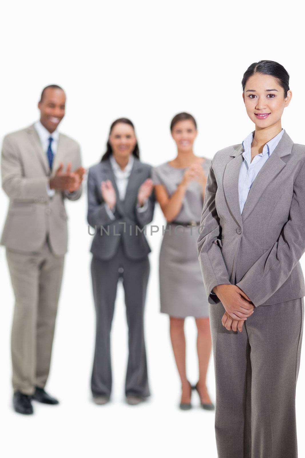 Close-up of a businesswoman smiling with co-workers applauding and looking at her in the background