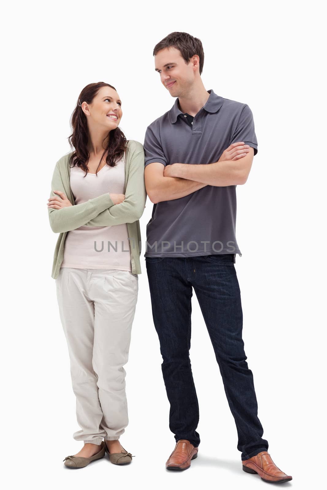 smiling couple looking at each other and crossing their arms against white background