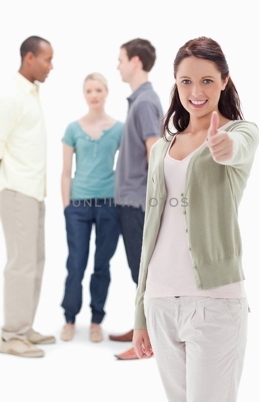 Girl smiling and giving the thumbs-up with friends chatting in background